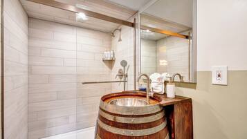A bathroom with a wooden barrel sink, a glass shower enclosure, and a large mirror.
