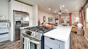 Una cocina moderna con refrigerador, estufa y horno de acero inoxidable. Hay un microondas sobre la encimera y una zona de comedor con mesa y sillas.