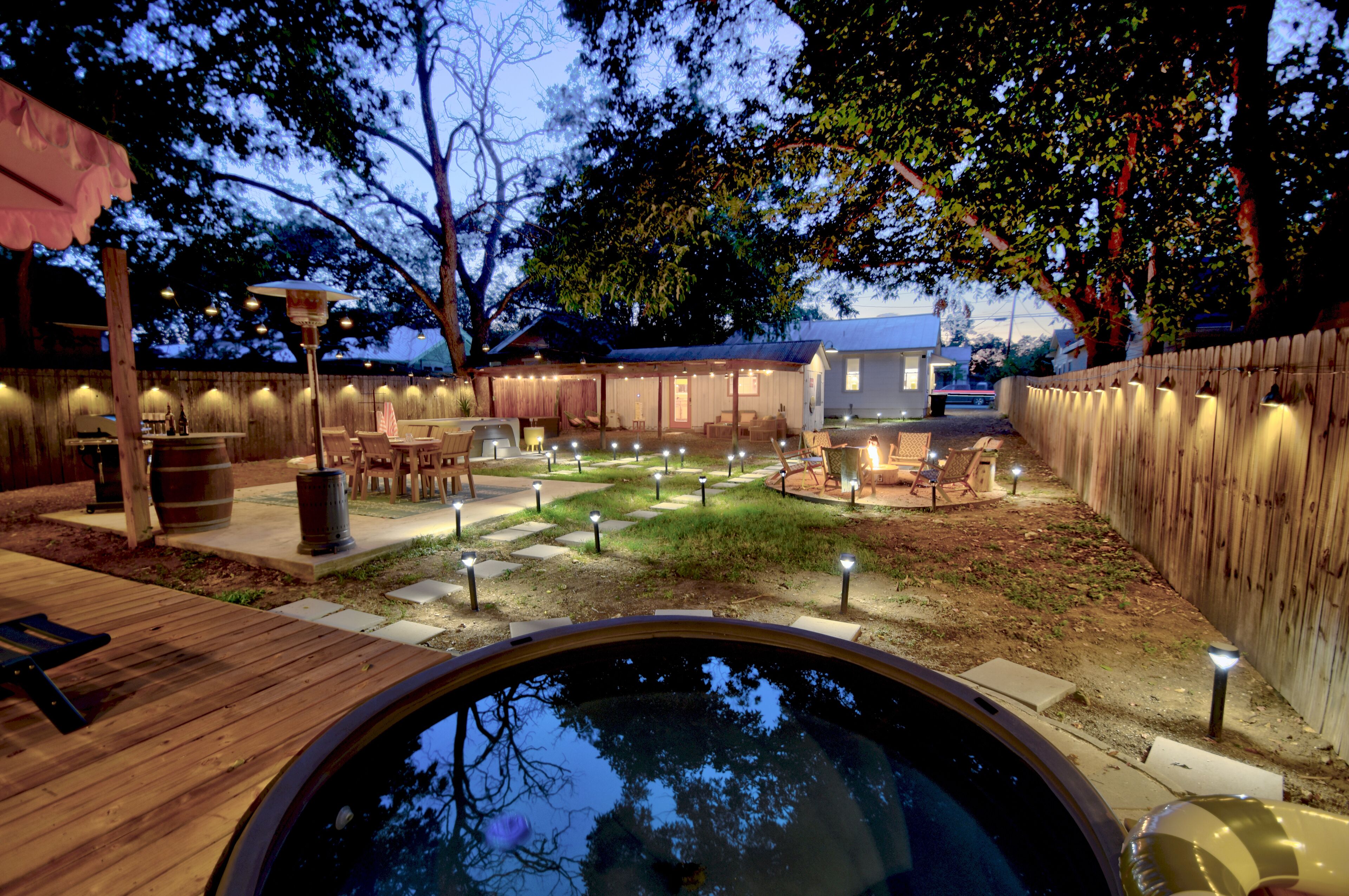 A backyard with a hot tub, wooden deck, and outdoor seating area with string lights.