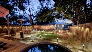 Un patio trasero con jacuzzi, terraza de madera y zona de estar al aire libre con luces colgantes.