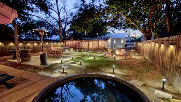 A backyard with a hot tub, wooden deck, and outdoor seating area with string lights.