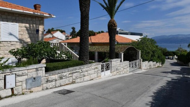 Una calle residencial con muros de piedra, una carretera pavimentada y una vista despejada del mar y las montañas al fondo.
