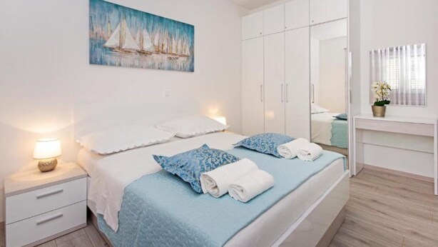 Ein Schlafzimmer mit Bett, Nachttischen, einem Bild, einem Kleiderschrank und einem Fenster mit Vorhängen.