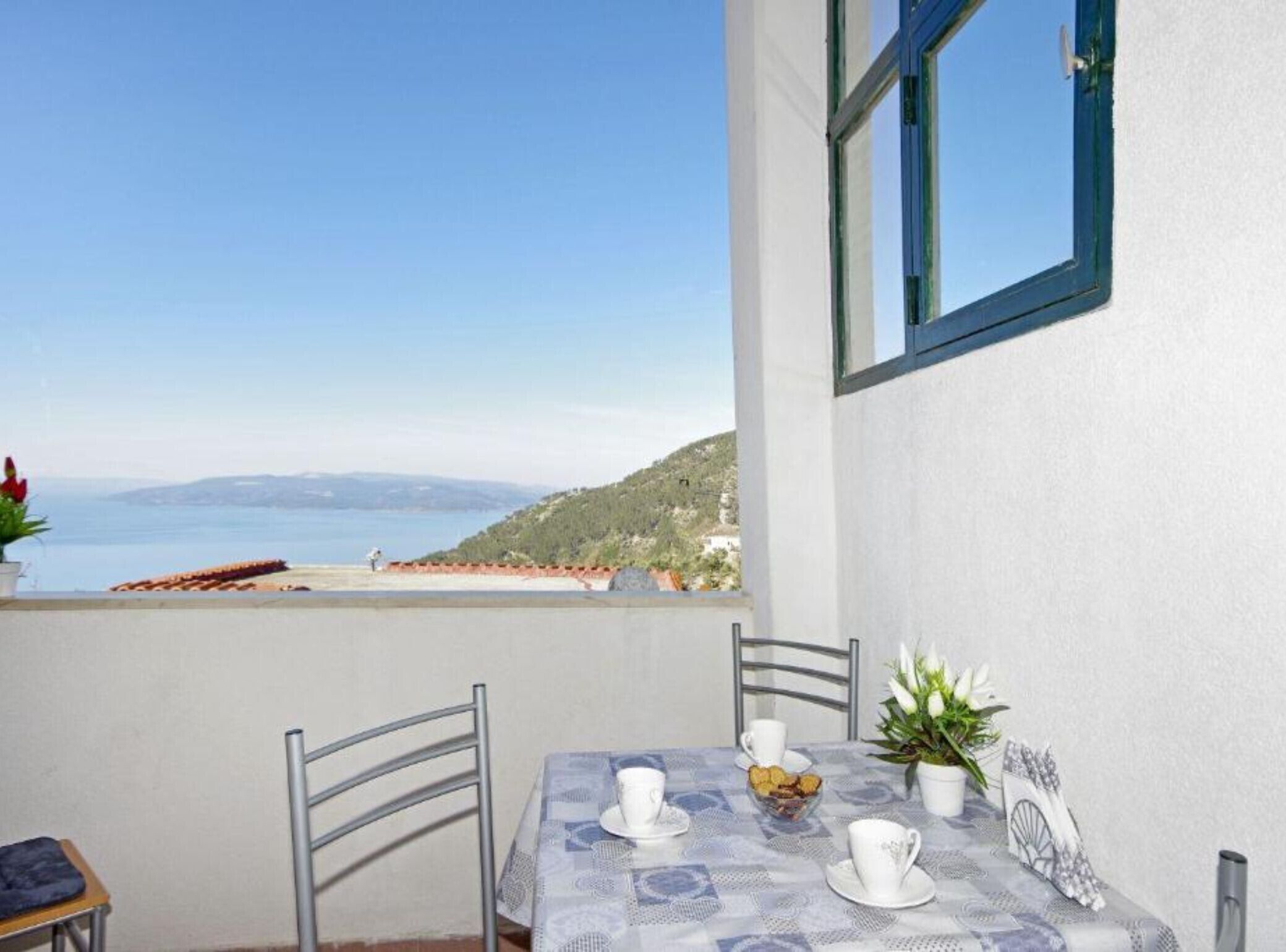 Un balcón con una mesa dispuesta para dos personas, con vista a una playa y al mar.