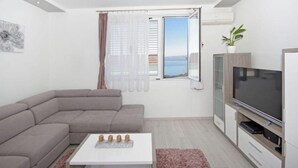 Ein modernes Wohnzimmer mit einem grauen Ecksofa, einem Flachbildfernseher und einem großen Fenster mit Meerblick.