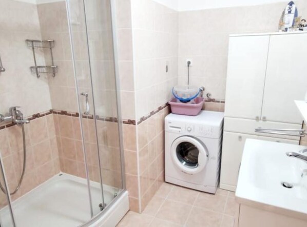 A bathroom with a glass-enclosed shower, a washing machine, a sink, and a cabinet.