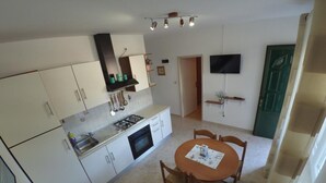 A compact kitchen with white cabinets, a gas stove, and a dining table with chairs. - Apartments Maritimo - Two Bedroom Apartment with Sea View and Terrace (Smokvica)