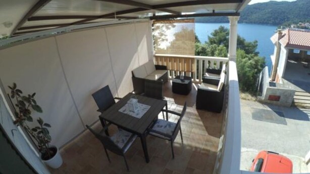 A balcony with a table and chairs, overlooking a body of water and hills. - Apartments Maritimo - Two Bedroom Apartment with Sea View and Terrace (Smokvica)