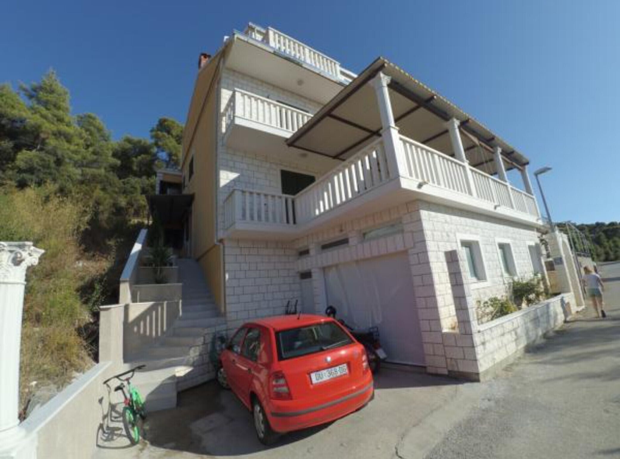 A two-story building with a balcony, a red car parked in front, and a bicycle leaning against the wall.