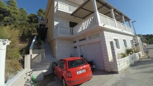 A two-story building with a balcony, a red car parked in front, and a bicycle leaning against the wall. - Apartments Maritimo - Two Bedroom Apartment with Sea View and Terrace (Smokvica)