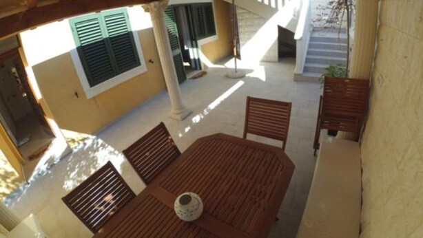 Une terrasse extérieure avec une table et des chaises en bois, un parasol blanc et un escalier menant à un niveau supérieur.