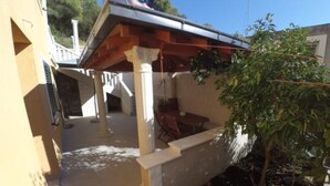 Un espace extérieur abrité, doté d’une table et de chaises, d’une structure en forme de pergola et offrant une vue sur un bâtiment en arrière-plan.