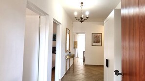 Un couloir orné d’un lustre, avec une porte en bois et un tableau encadré accroché au mur.