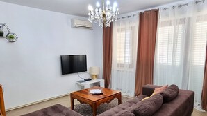 Un salon avec un canapé, un téléviseur, une lampe et un lustre.