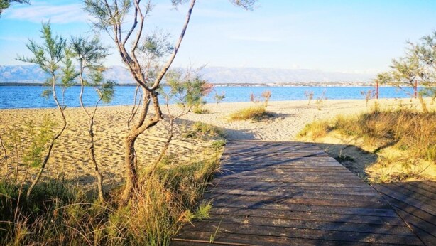 A wooden pathway leading to a beach with sparse vegetation and a clear view of the sea and distant mountains. - Villa Casa Mia Sabunike A2 (Privlaka)