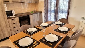 A dining room with a wooden table set for four, equipped with plates, cutlery, and glasses. There are four chairs around the table, and a kitchen area with cabinets and a microwave is visible in the background. - Villa Casa Mia Sabunike A2 (Privlaka)