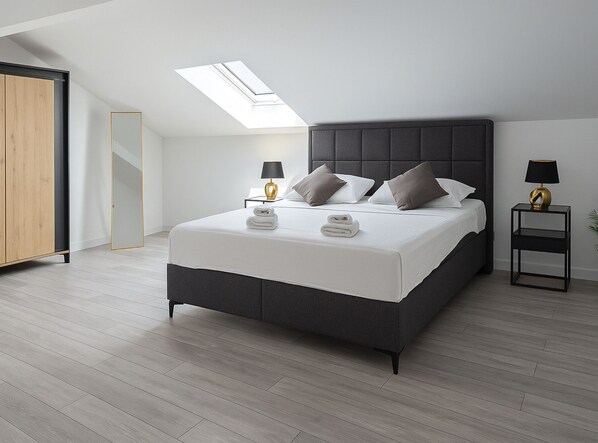 A modern bedroom with a skylight, a bed with pillows, a nightstand, and a wardrobe.