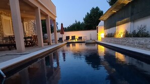 A swimming pool with a stone wall on one side and a covered patio area with chairs and tables. - Villa Casa Mia Sabunike A3 (Privlaka)