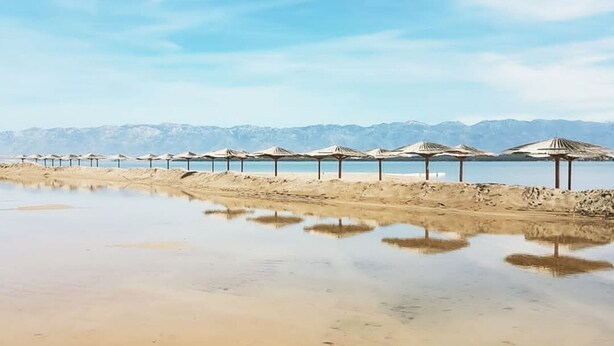 A beach with rows of umbrellas and a calm water body reflecting the sky. - Villa Casa Mia Sabunike A3 (Privlaka)