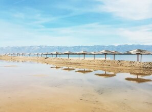 A beach with rows of umbrellas and a calm water body reflecting the sky.