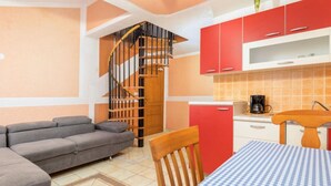 A compact living space with a sofa, a dining table with a checkered tablecloth, a kitchen area with red cabinets, and a spiral staircase. - Apartments Manda - One Bedroom Apartment With Terrace (A1) (Fazana)