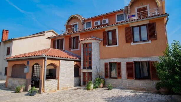 A two-story building with a stone facade, multiple windows with shutters, and a tiled roof.