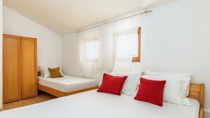 A room with a large bed, a smaller bed, a wardrobe, and a window with curtains.