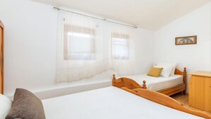 Ein Schlafzimmer mit zwei Betten, einem Holzschrank und einem Fenster mit durchsichtigen Vorhängen.