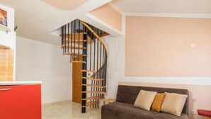 Un espace de vie compact comprenant un canapé marron, un meuble rouge et un escalier en colimaçon.