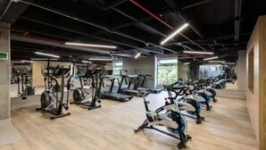 A gym with various cardio machines, wooden flooring, and a high ceiling with exposed beams. - The Remote Work Dream (Medellín)