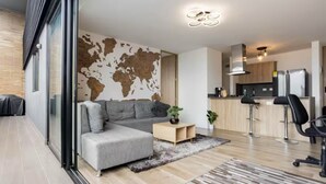 A modern living room with a grey sectional sofa, a world map wall, a kitchen area with stainless steel appliances, and a sliding glass door leading to a balcony. - The Remote Work Dream (Medellín)
