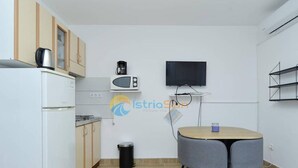 A compact kitchen with a refrigerator, microwave, stove, and a small trash bin. There's a TV mounted on the wall and a round table with two chairs. - Apartments Manda - One Bedroom Apartment With Terrace (A5) (Fazana)