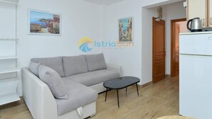 A modern living room with a sofa, a small black table, and a white refrigerator. There are two framed pictures on the wall and a logo for 'IstriaSun'. - Apartments Manda - One Bedroom Apartment With Terrace (A5) (Fazana)
