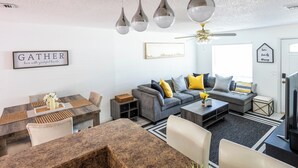 Een moderne woonkamer met een grijze bank, een eettafel en een plafondventilator.