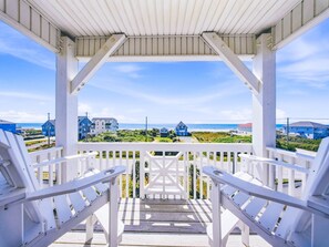 Une véranda couverte avec des balustrades blanches, d’où l’on a une vue sur la plage et les maisons.