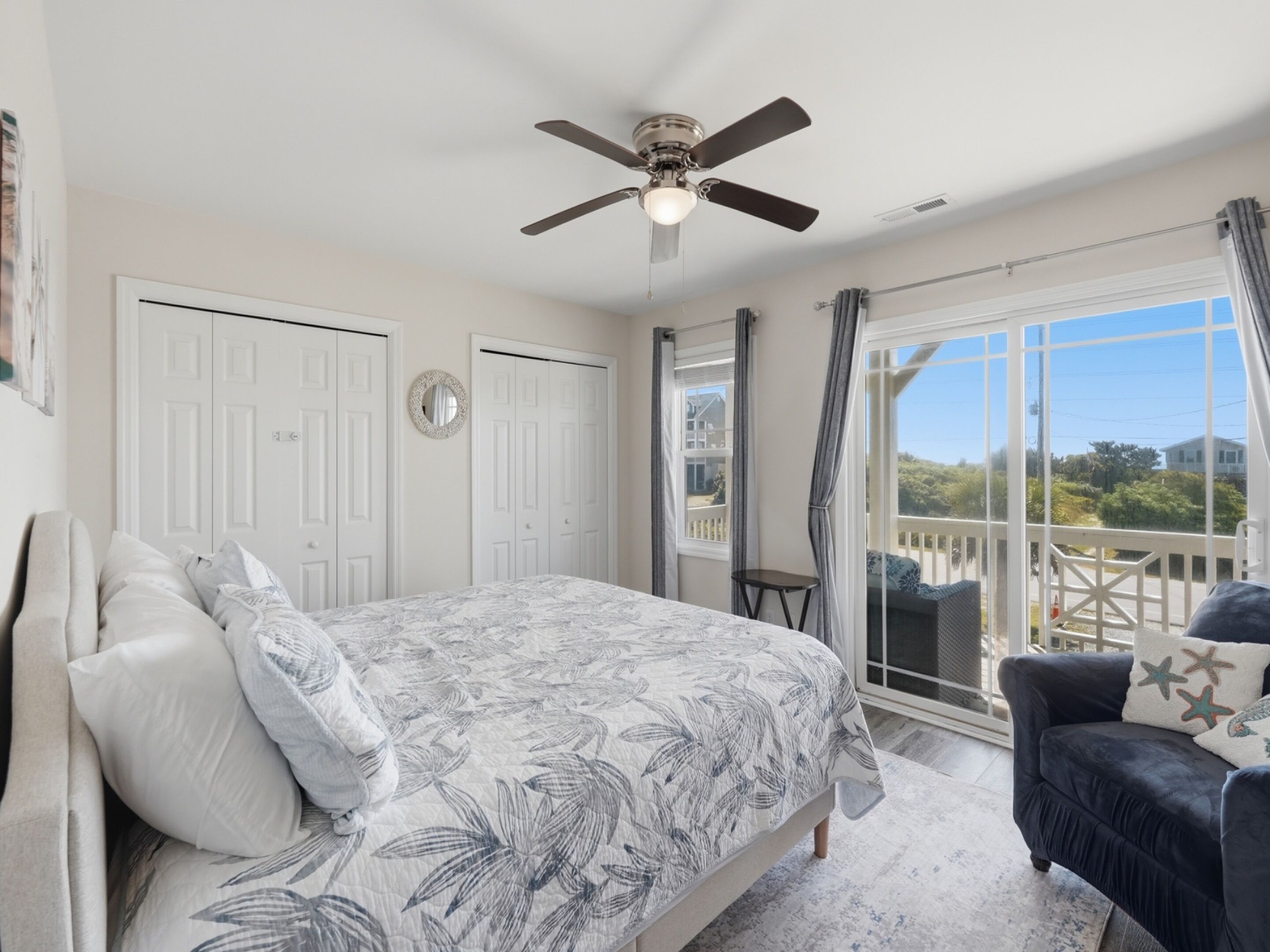 A bedroom with a bed, a ceiling fan, a window with curtains, and a view of the outside.