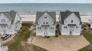 Une propriété située en bord de mer, comprenant trois grandes maisons, une allée et une plage en arrière-plan.