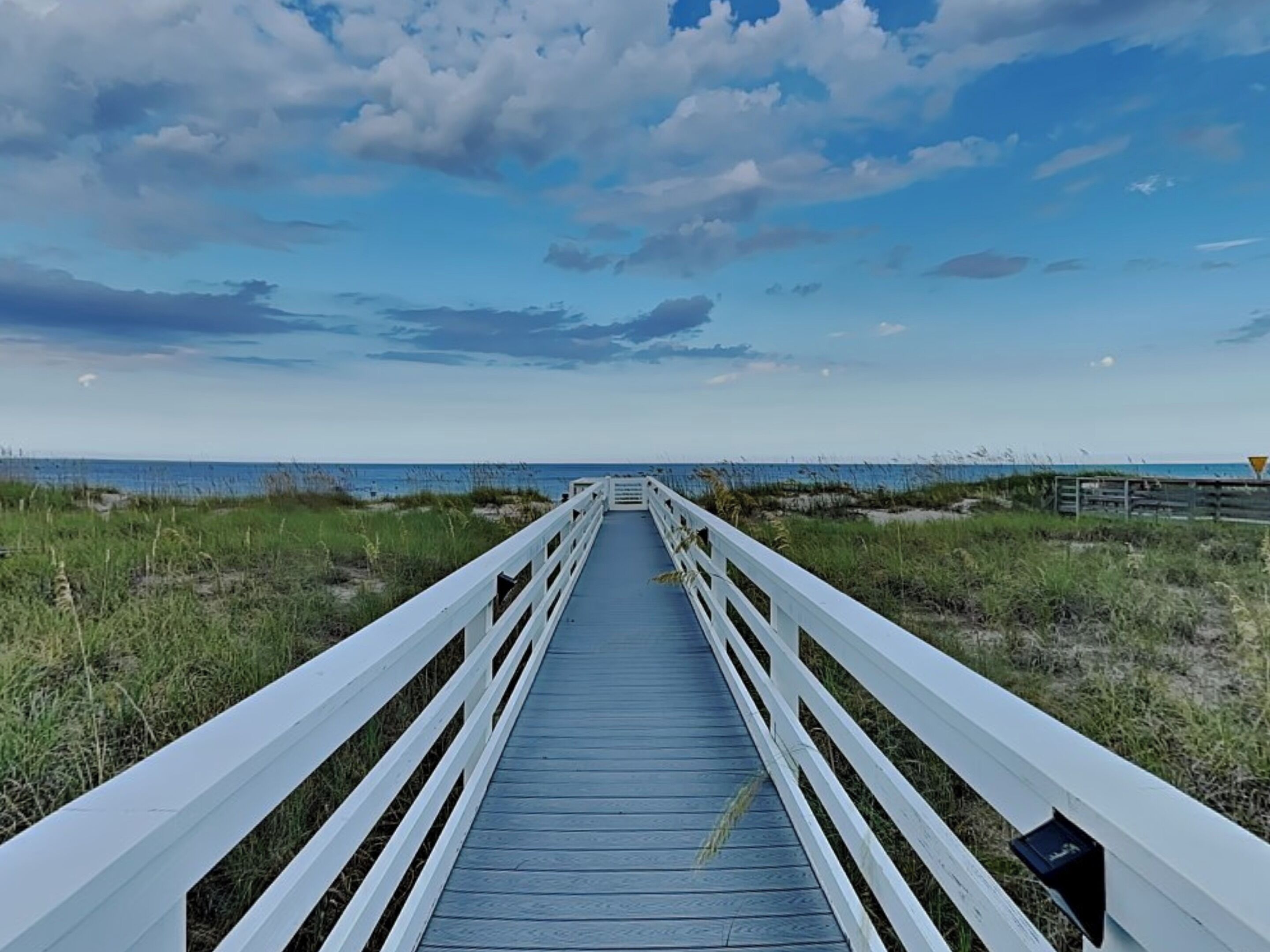 A wooden boardwalk leading to a beach with a clear sky.