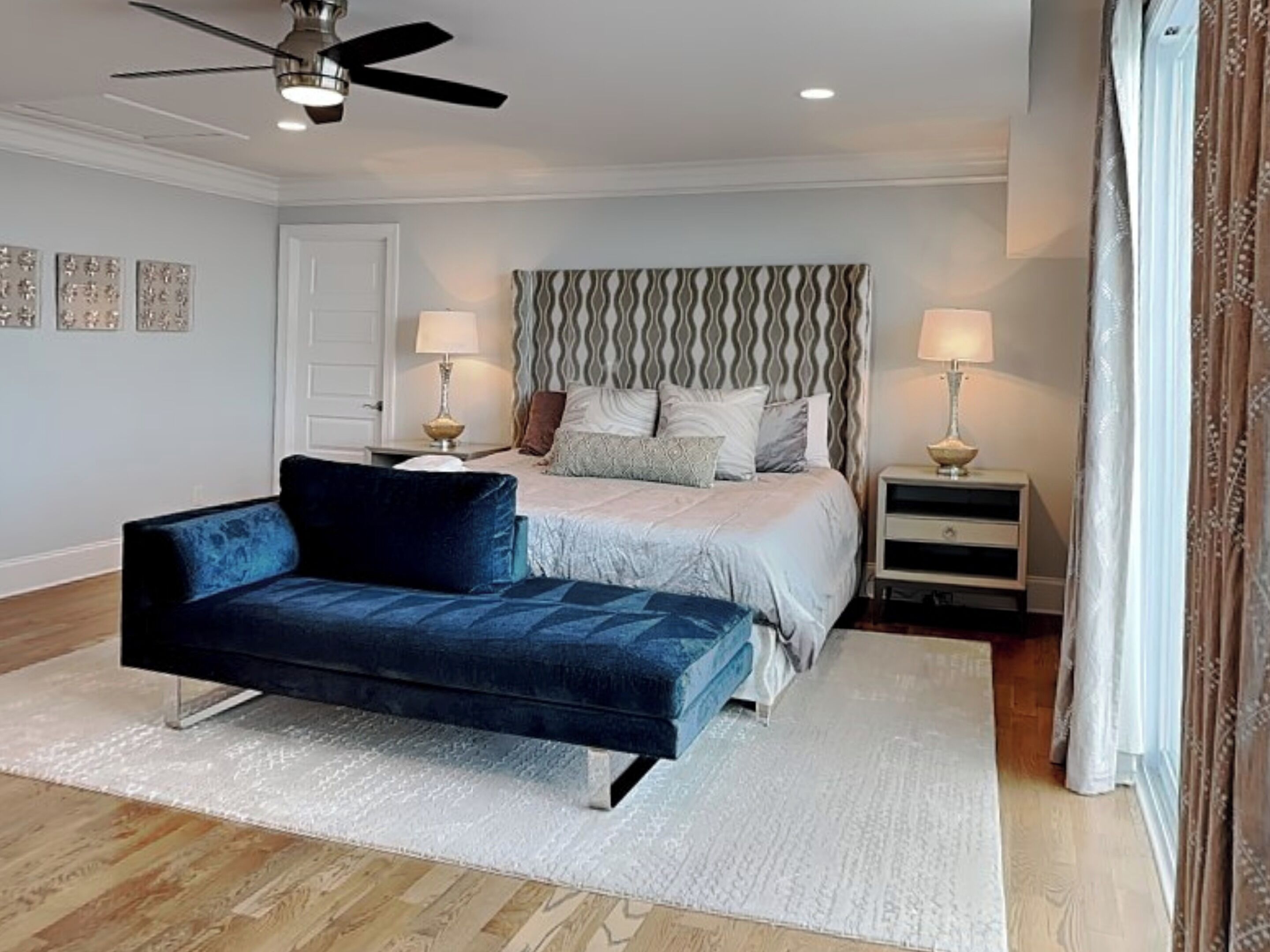 A bedroom with a bed, a blue sofa, two bedside tables, a ceiling fan, and a door.