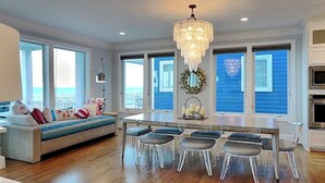 A modern kitchen with a dining area, large windows, and a chandelier. - Southern Comfort by Carolina Retreats (Kure Beach)