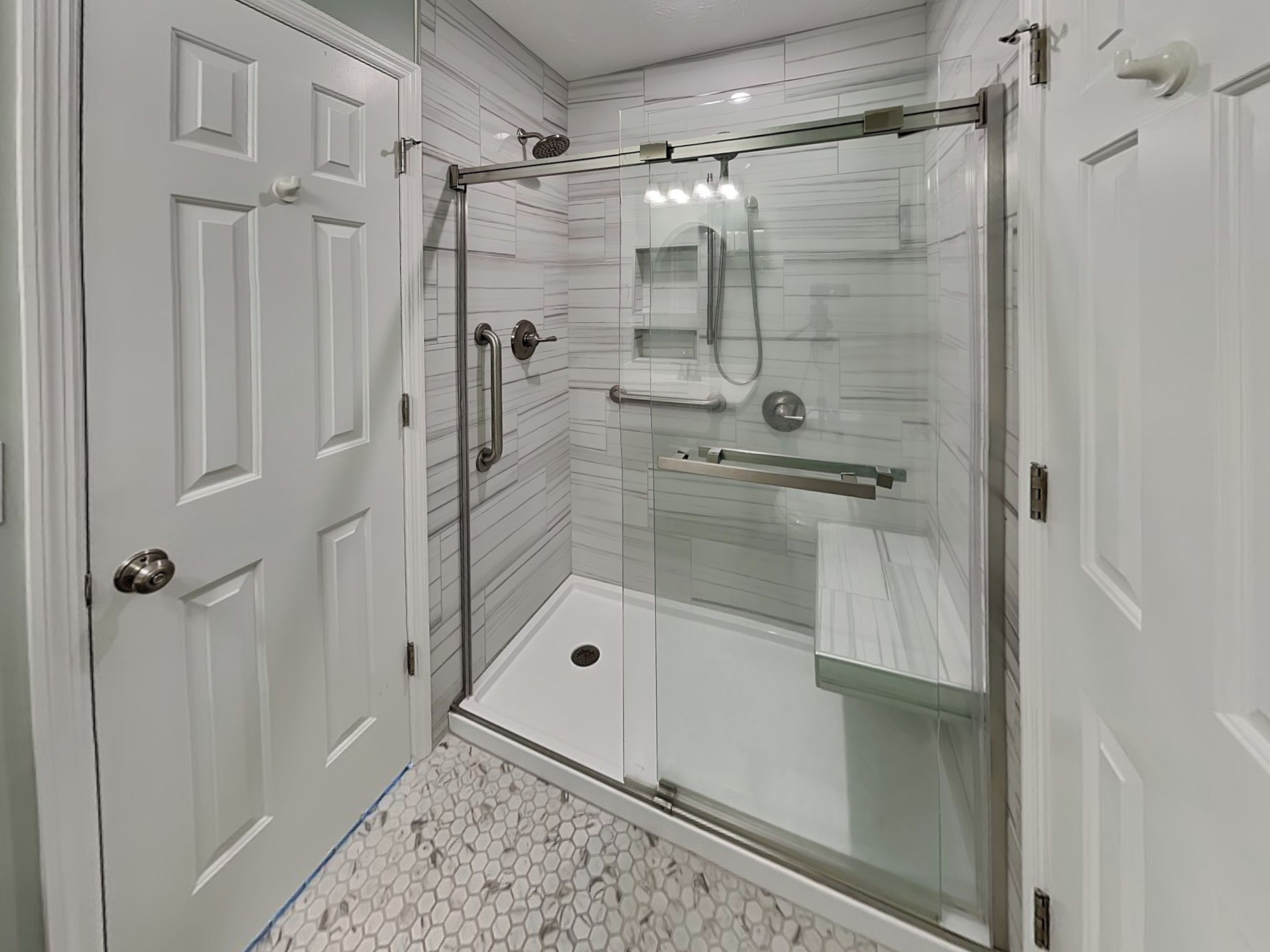 A modern bathroom with a glass shower enclosure, white tiled walls, and a hexagonal tile floor.