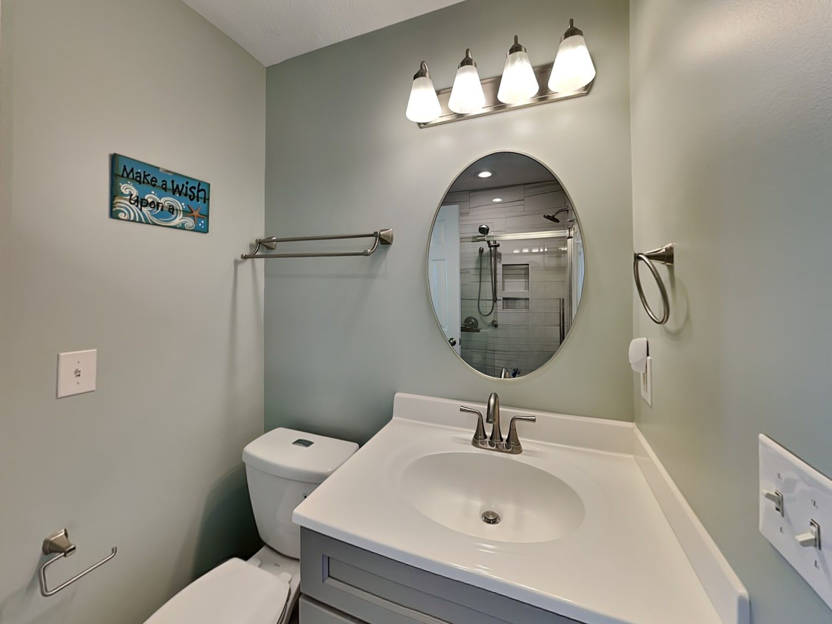 A bathroom with a white sink, a round mirror, a towel rack, a toilet, and a wall-mounted light fixture.