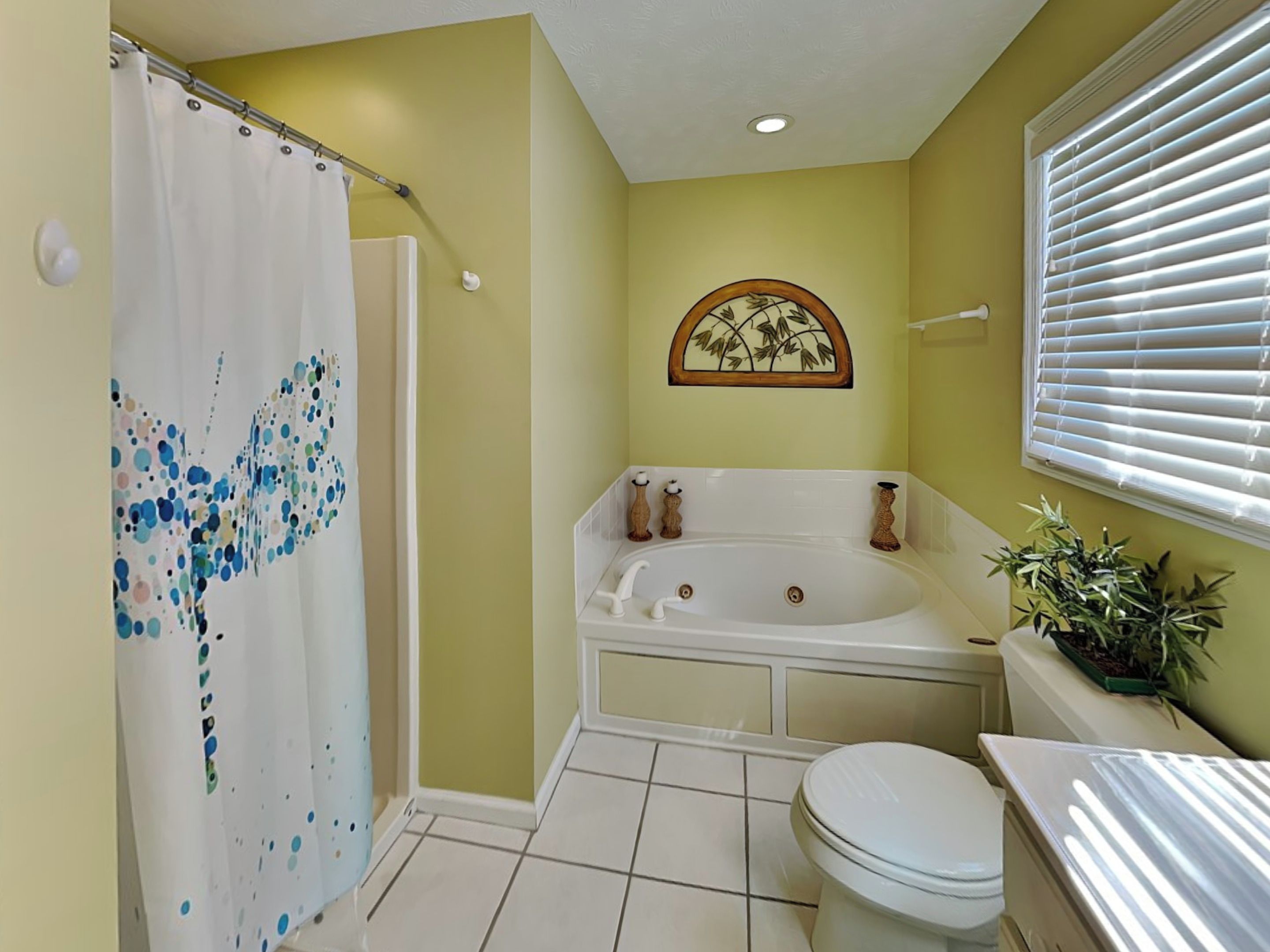 A bathroom with a shower curtain, bathtub, toilet, and a window with blinds.
