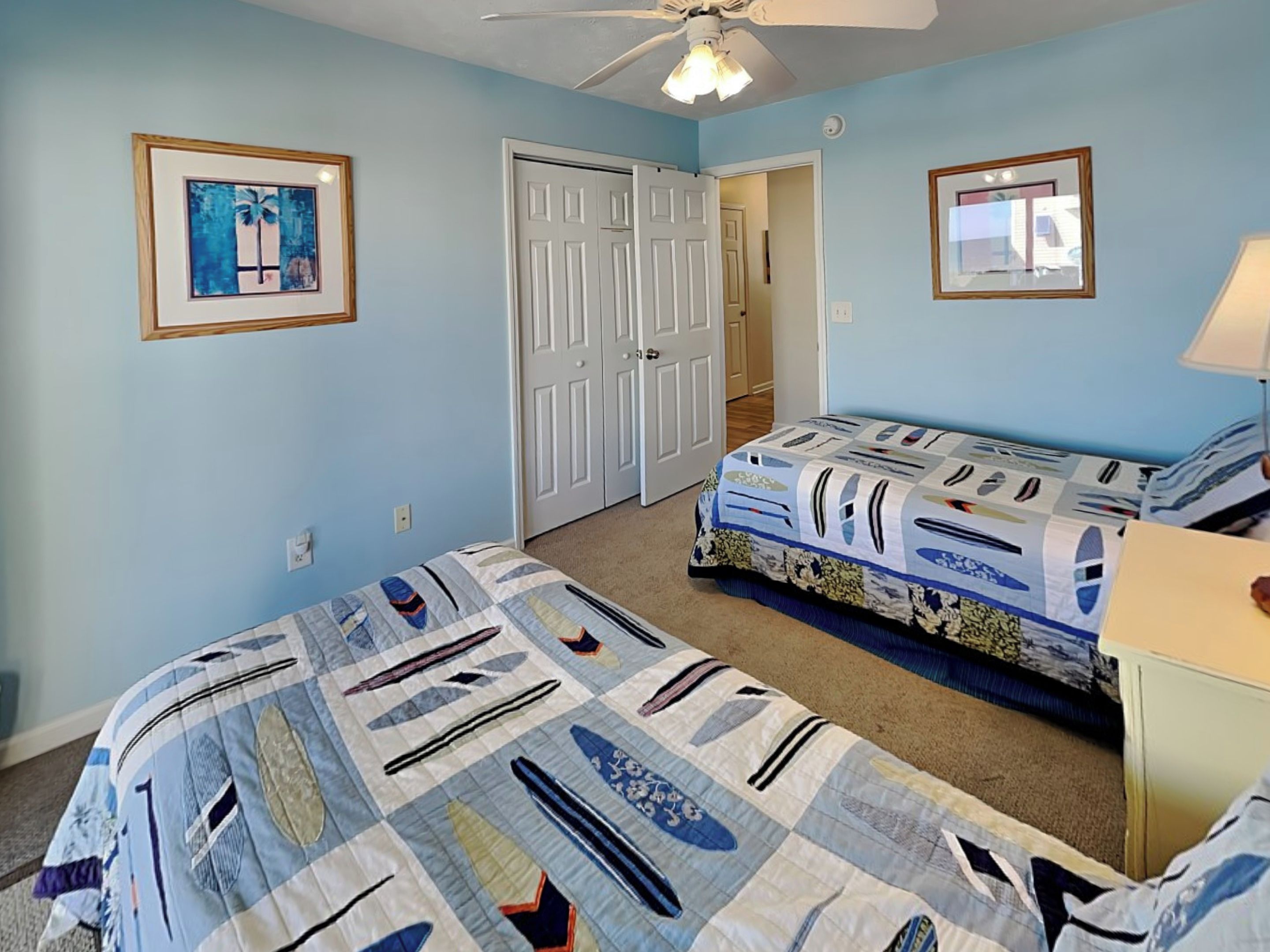 A bedroom with two beds, a ceiling fan, and a door leading to another room.