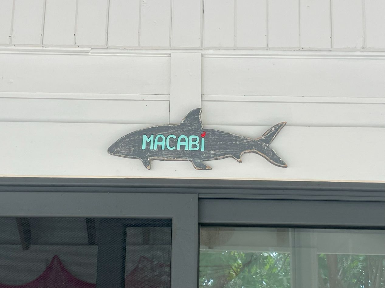 Um sinal em formato de tubarão com a palavra 'MACABI' em um edifício.