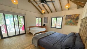 A bedroom with a large bed, a smaller bed, a ceiling fan, and a view of the outdoors. - Sol y Arena Xcalak (Xcalak)