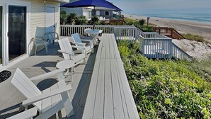 A wooden deck with white chairs and a table, overlooking a beach. - Riptide by Topsail Realty (Holly Ridge)