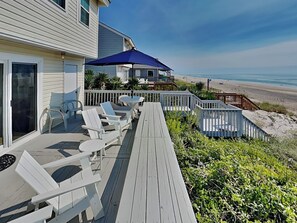 A wooden deck with white chairs and a table, overlooking a beach. - Riptide by Topsail Realty (Holly Ridge)