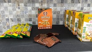Un comptoir de cuisine sur lequel se trouvent divers produits alimentaires emballés, notamment une boîte étiquetée « AKOMA, noix de cajou grillées à sec » et plusieurs boîtes de jus d’ananas « Eku Pina ».