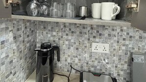 Une cuisine compacte équipée d’une machine à café, d’une bouilloire et d’un four à micro-ondes, le tout posé sur le plan de travail.